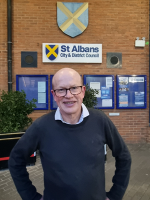 Paul de Kort is standing in front of the St Albans District Council building, with the sign visible behind him. He is looking directly at the camera and smiling.