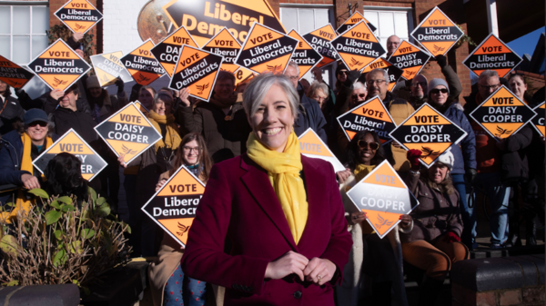 Photo of Daisy Cooper in front of a group of campaigners holding yellow diamonds 